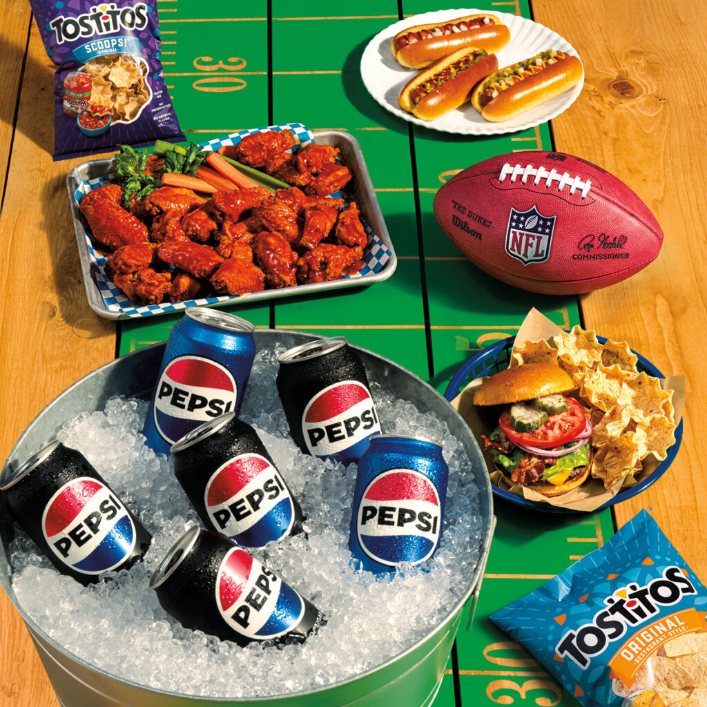 Table filled with Pepsi on ice, Tostitos, Hot Dogs, Wings, Nachos and NFL Football